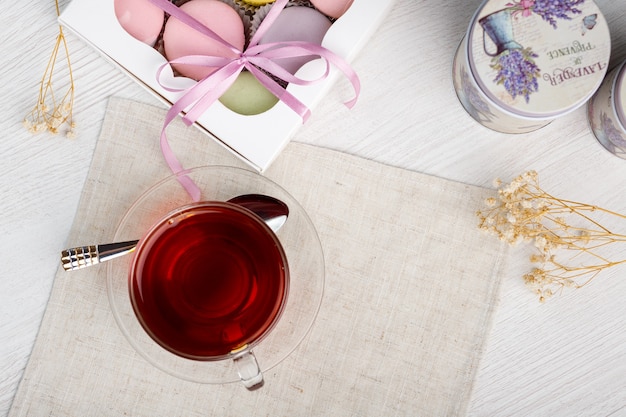 Multicolored macaroons and a cup of tea on a light wooden table Morning tea and sweets Top view