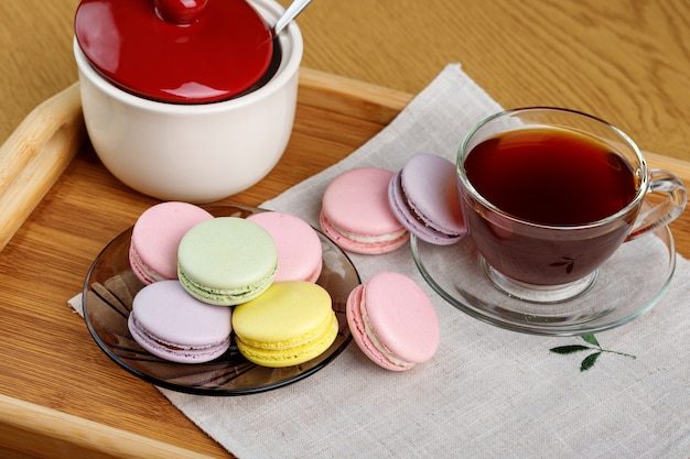 Multicolored macaroons and a cup of tea on a wooden tray Morning tea and sweets