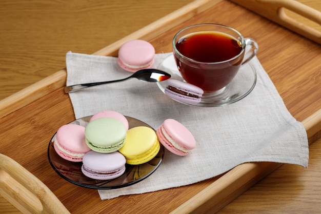 Multicolored macaroons and a cup of tea on a wooden tray Morning tea and sweets