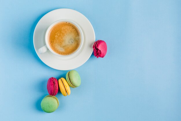 Multicolored macaroons with a white Cup of coffee on a blue copyspace, top view, flat lay with copyspace