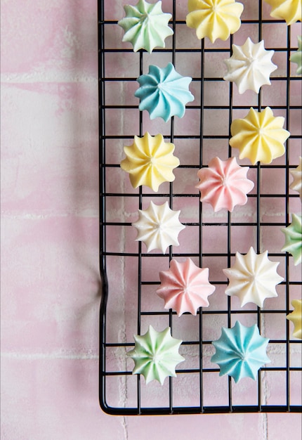 Multicolored meringue on a baking rack on a pink tile background