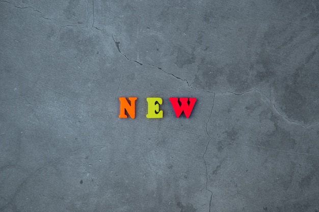 The multicolored new word is made of wooden letters on a grey plastered wall.