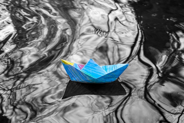 Multicolored origami paper boats in stream or puddle on black background A symbol of childhood or piece of light in dark world