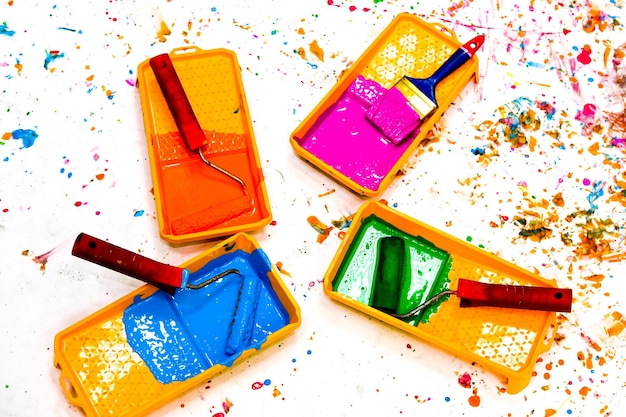 Фото Разноцветная краска в лотках с валиками на белом фоне, вид сверху