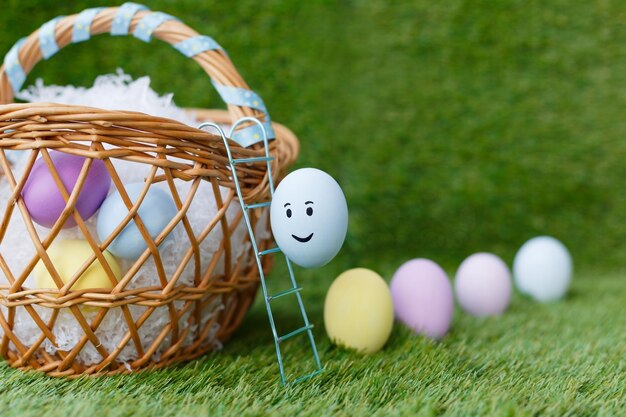 Foto uova di gallina di pasqua dipinte multicolore con occhi bocca rosa giallo salire le scale in un cesto di vimini su erba verde simboli per la celebrazione della festa religiosa per cristiani e cattolici