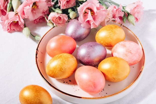 Разноцветные окрашенные пасхальные яйца в пастельных тонах в тарелке на белой хлопчатобумажной скатерти