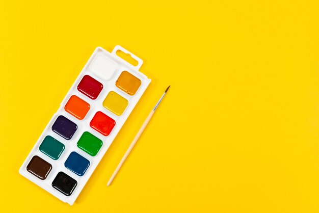 Multicolored paints and paintbrush on a yellow background back to school