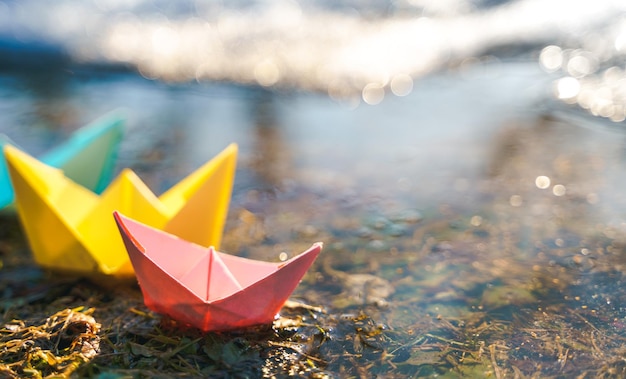 Multicolored paper boats colorful pink yellow blue orange ships in big spring snow puddle on winter street warm wet rainy weather old grass hello spring autumn children play have fun outdoors