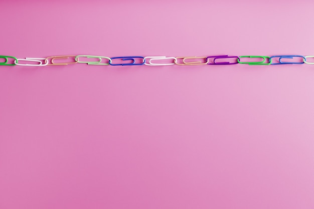 Multicolored paper clips are attached in a row on a pink background