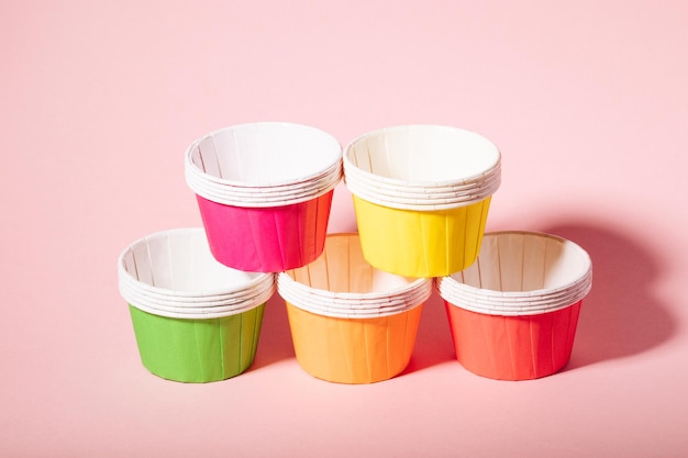 Multicolored paper molds for muffins and cupcakes on a pink background