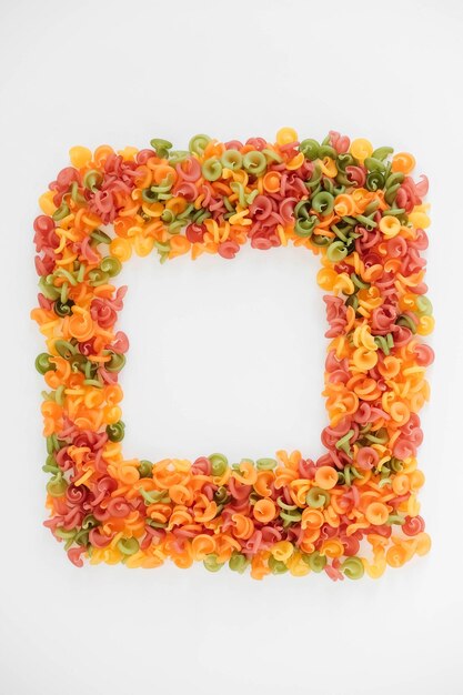 Multicolored pasta scattered on a white background in the form of a frame