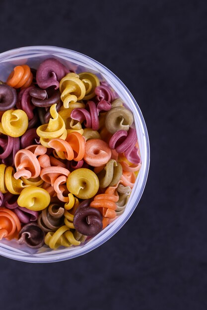 Multicolored pasta with the addition of natural vegetable dye In a jar on a black concrete table. Top view, .