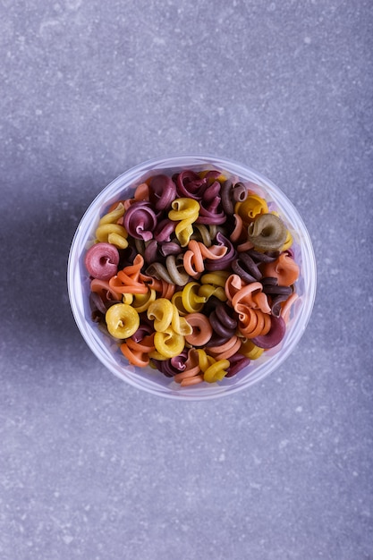 Photo multicolored pasta with the addition of natural vegetable dye. in a jar on a concrete table