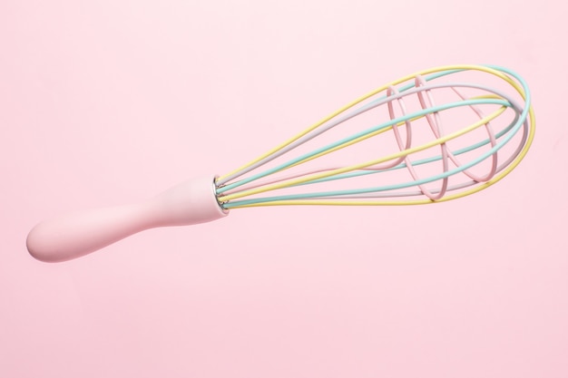 Multicolored pastel kitchen whisk on pink