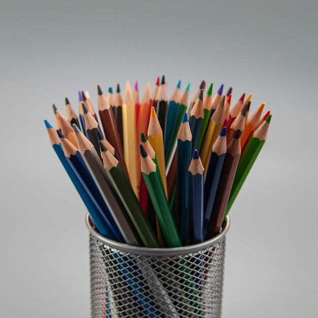 Multicolored pencils are laid out in a gray metal glass on a gray square