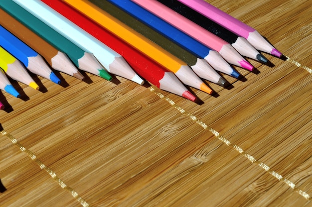 Разноцветные карандаши, выложенные дугой на соломенном фоне.