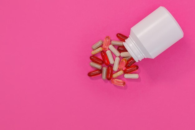 Multicolored pills and capsules on a pink background