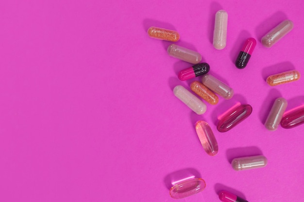 Multicolored pills and capsules on a pink background