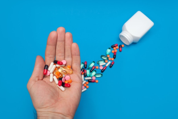 Разноцветные таблетки в руке на синем фоне