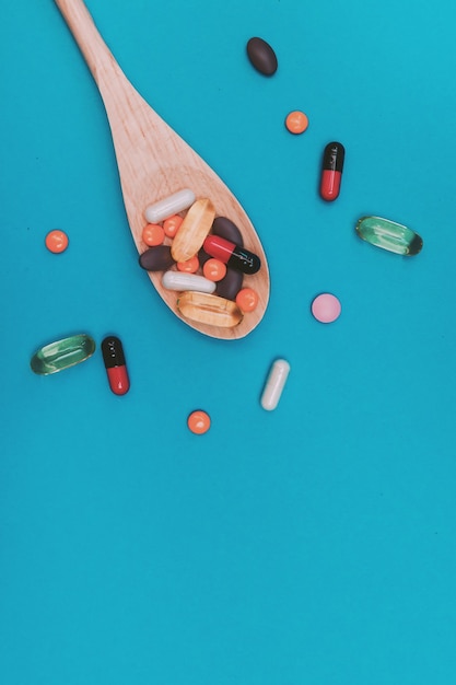 Разноцветные таблетки в деревянной ложке на синем фоне