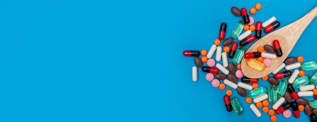 Разноцветные таблетки в деревянной ложке на синем фоне панорамы
