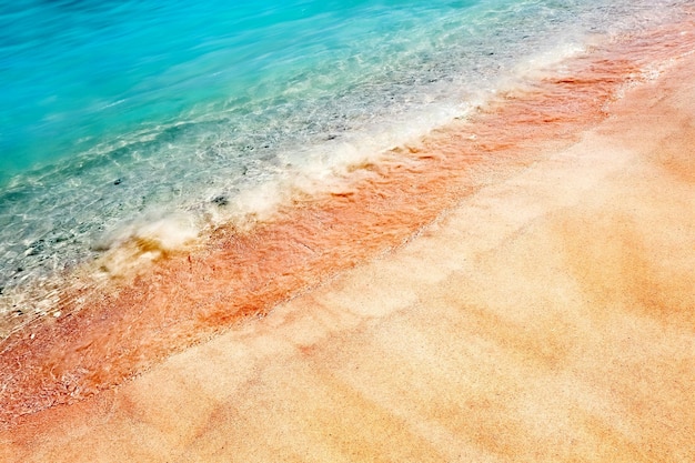 Multicolored pink sand and blue water on a deserted red beach tropical sand background