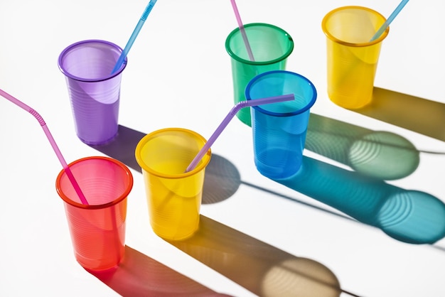 Photo multicolored plastic cups with drinking straws, isolated on white background. light and shadow.