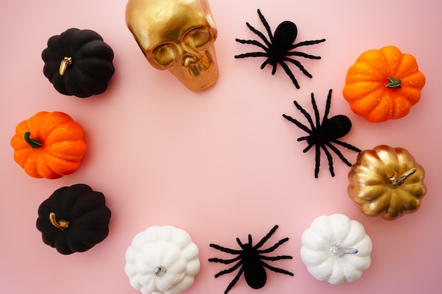 Multicolored pumpkins, a golden skull and black spiders lie on a pink background