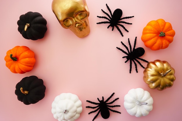 Multicolored pumpkins a golden skull and black spiders lie on a pink background