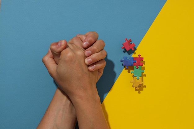 Multicolored puzzle pieces on a blueyellow background with hands