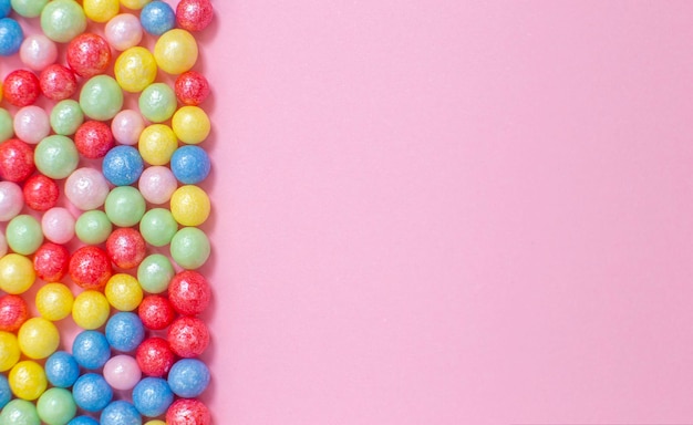 Multicolored round glossy balls of sugar confectionery topping lie on a pink background