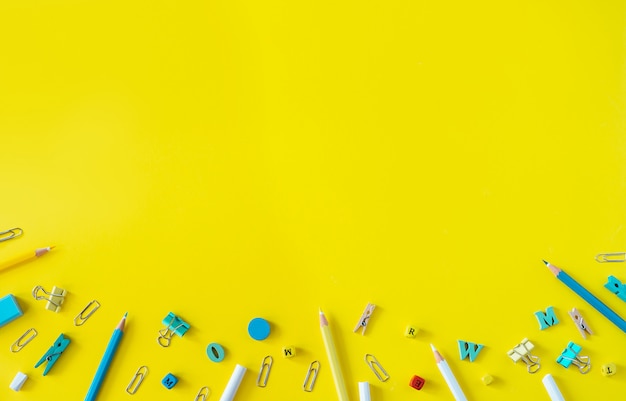 Multicolored school supplies on yellow background with copy space