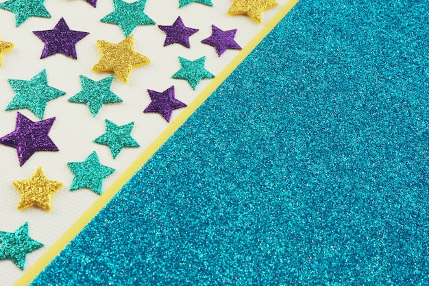 Multicolored shiny stars on gray textured paper and a strip of yellow and blue shiny paper