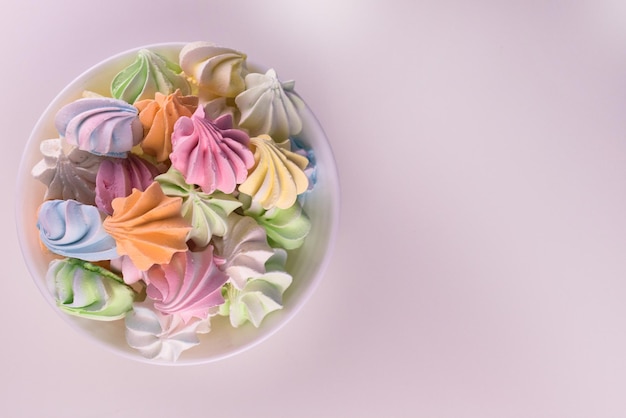 Multicolored small meringues in a plate on a white background View from the top Copy space