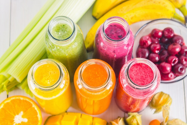 Multicolored smoothies in bottles of mango, orange, banana, celery, berries, on a wooden table.