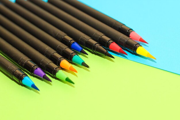 Разноцветные канцелярские фломастеры и кисти на фоне разноцветной картонной бумаги