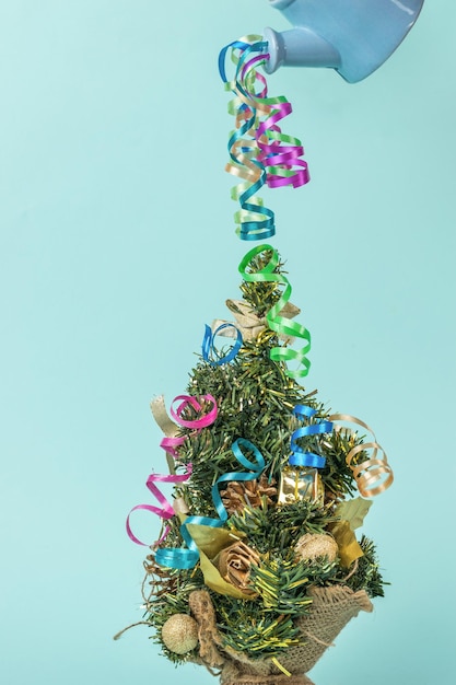 Multicolored streamers flowing out of the watering can on the Christmas tree. The minimum concept of the New Year. Contemporary art. Place for text.