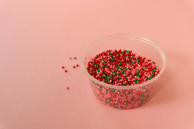 Multicolored sweet sprinkles in bowl on a pink background.