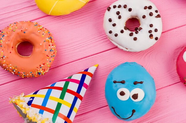 Multicolored sweets on pink wooden table. Colorful Birthday party background with donuts and party hats. Concept of holiday celebration.