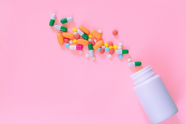 Multicolored tablets pills capsules in plastic bottle on pink background copy space