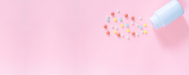 Multicolored tablets pills capsules in plastic bottle on pink background copy space