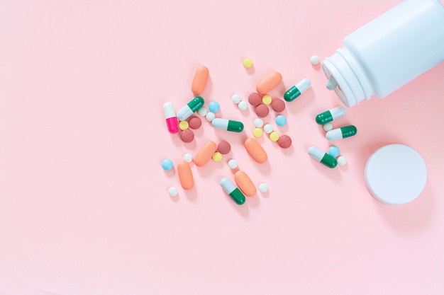 Multicolored tablets pills capsules in plastic bottle on pink background copy space