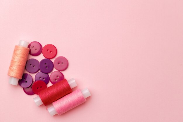 Multicolored thread spools and buttons on pink background