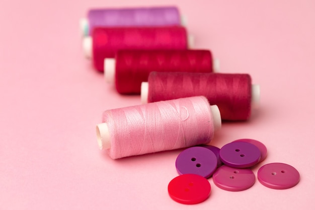 Multicolored thread spools and buttons on pink surface