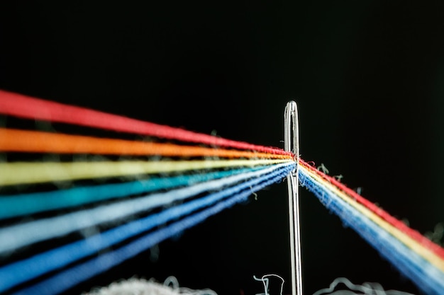 Multicolored threads for sewing in the form of a rainbow pass through an antique needle on a black background