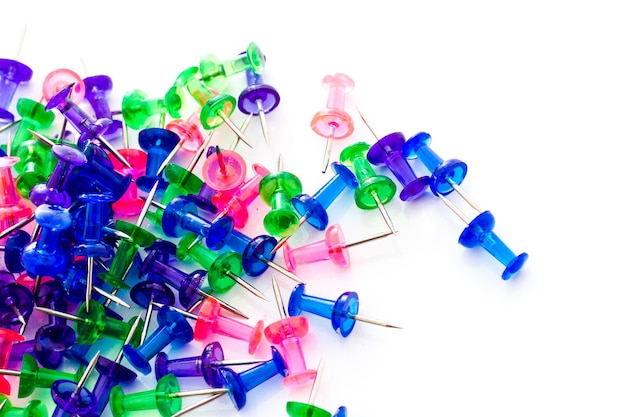 Multicolored thumbtacks in a pile on a white background.