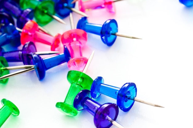 Multicolored thumbtacks in a pile on a white background.