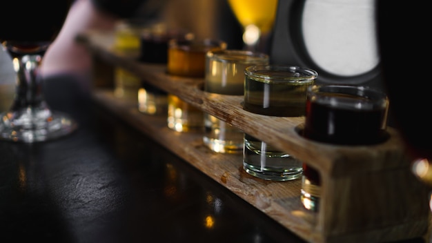 Multicolored transparent cocktails, a set of shots in one row, six servings on a wooden stand, substrate. Drink for the menu restaurant, bar, cafe