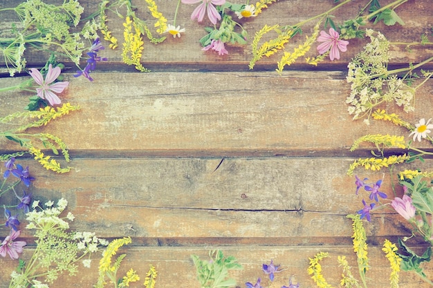 Multicolored wildflowers are arranged in a circle on a wooden table background Chamomile sweet clover wild geranium bluebells parsley inflorescences Horizontal boards Romantic Provence style