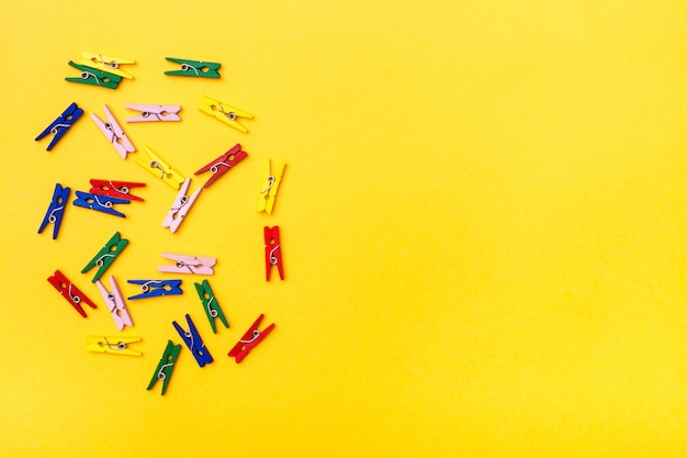 Multicolored wooden clamps lie chaotically on a yellow 